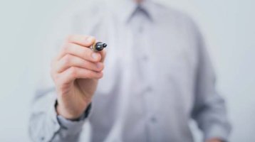 Ein Mann in einem Hemd, der einen Edding in der Hand hält und mit dem Edding zur Kamera zeigt.
